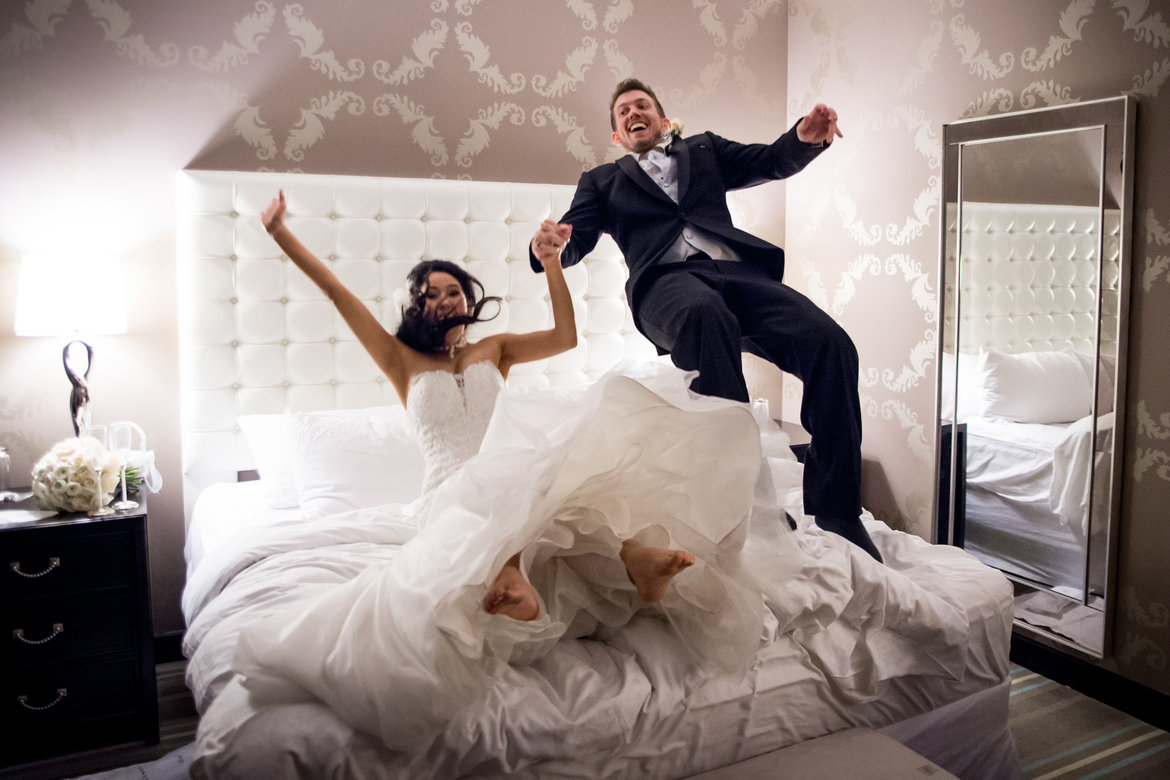 bride and groom jumping on bed