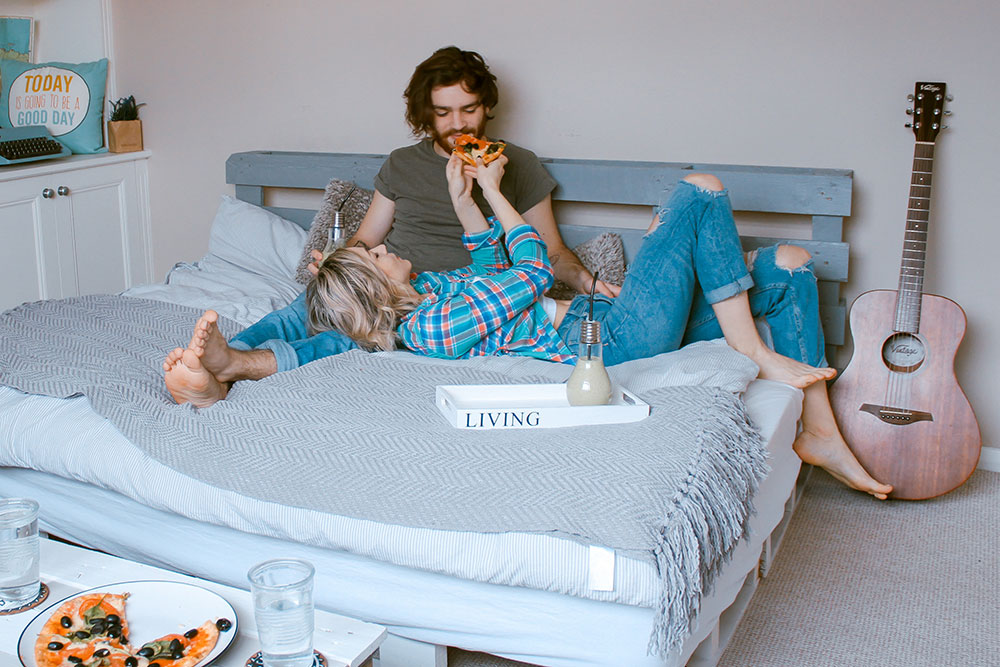 happy couple eating pizza in bed