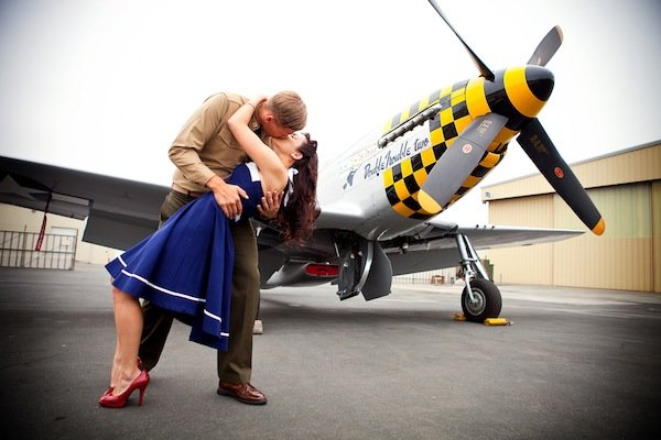 couple kissing in front of a plane 
